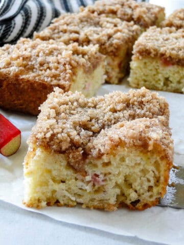 Close up side view of one piece of rhubarb coffee cake in front of more slices.