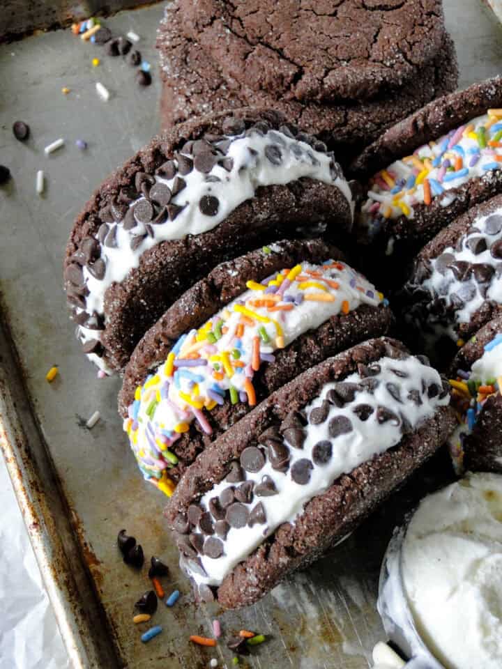 Ice cream cookie sandwiches rolled in mini chocolate chips and sprinkles on their side on sheet pan.