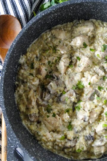 Creamy chicken orzo in large round skillet with wood serving spoon on the side.