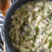 Creamy chicken orzo in large round skillet with wood serving spoon on the side.