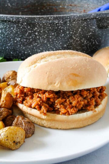 Side view of ground turkey sloppy joe on plate with potatoes sitting in front of skillet.