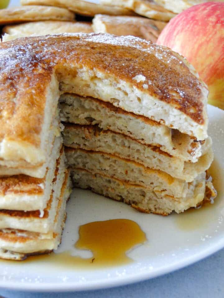 Close up side view of stacked pancakes on plate with wedge cut out.