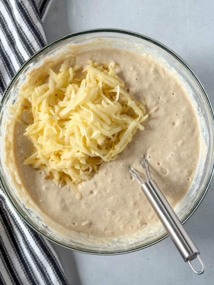 Grated apple added to pancake batter in large glass bowl.