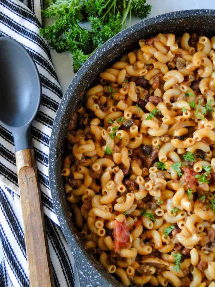 Close up top view of chili mac with leftover chili in skillet with serving spoon on the side.