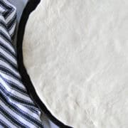Top view of easy homemade pizza dough stretched out on round pizza stone.