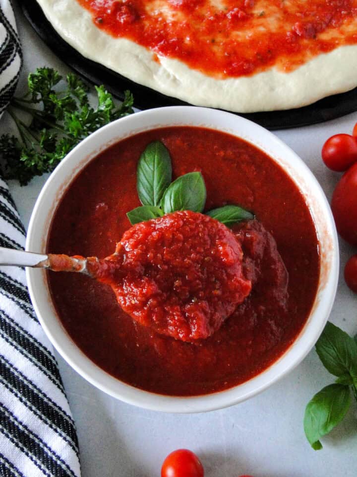 Easy pizza sauce recipe in bowl being scooped out with spoon.