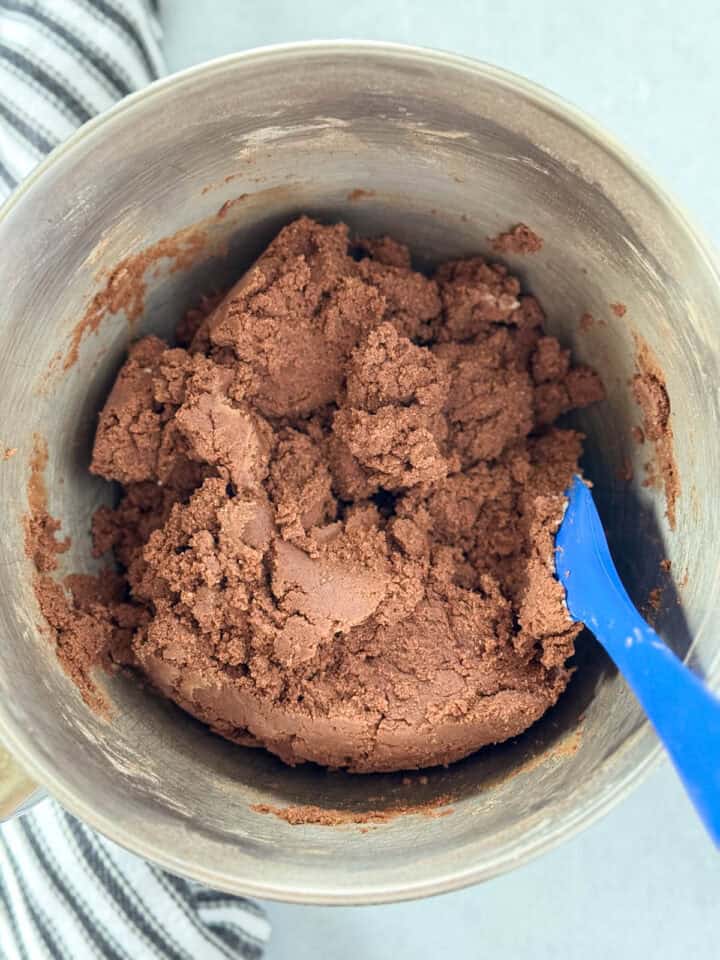 Dry ingredients mixed into wet in large metal mixing bowl with blue spatula.