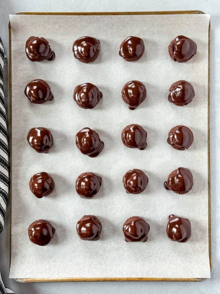 Fudge topping added on top of cherries on cookie sheet.