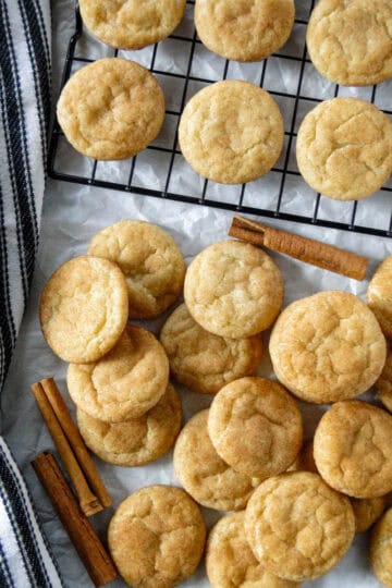 Top view of snickerdoodle cookies in a pile in front of wire rack with more cookies on it.