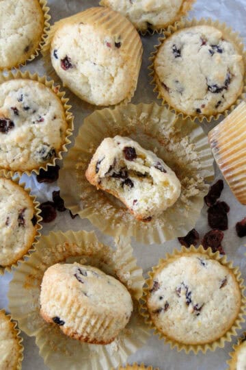 Top view of dried cranberry orange muffins on parchment paper with center muffin unwrapped and bite taken out of it.