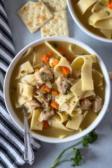 Close up top view of turkey noodle soup in white round bowl with spoon.