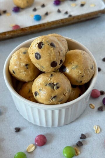 Monster cookie protein balls piled in white bowl sitting in front of pan of more protein balls.