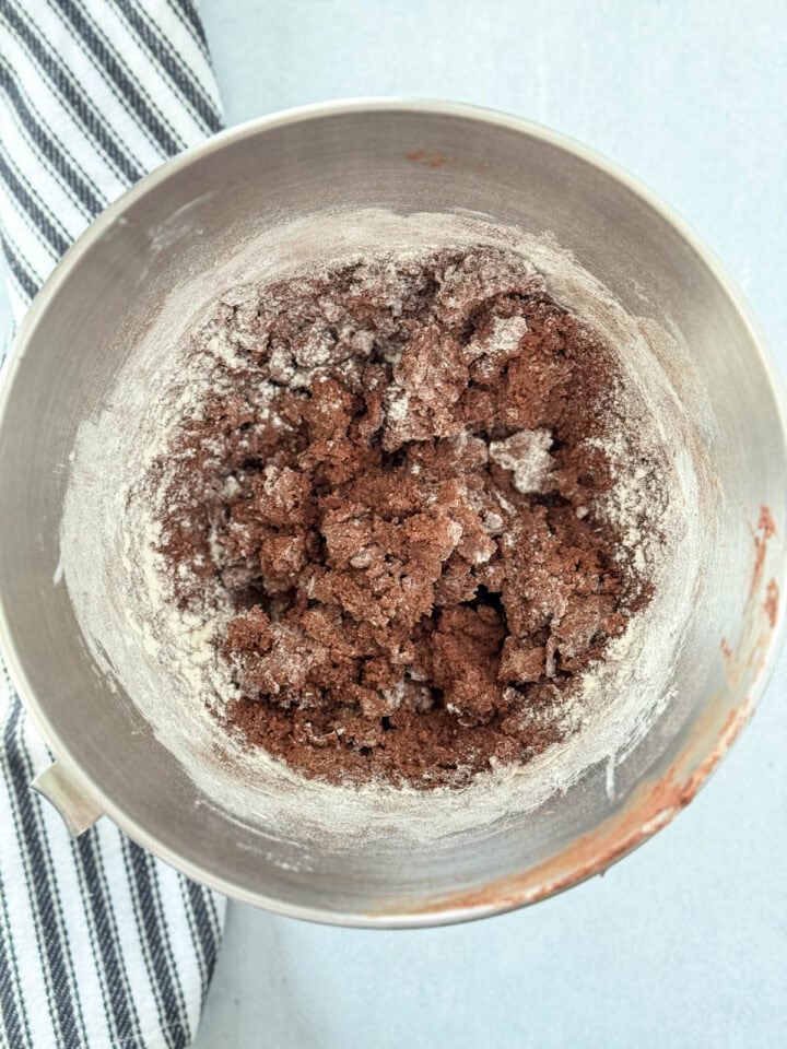Half of dry ingredients added to creamed butter and sugars in large metal mixing bowl.
