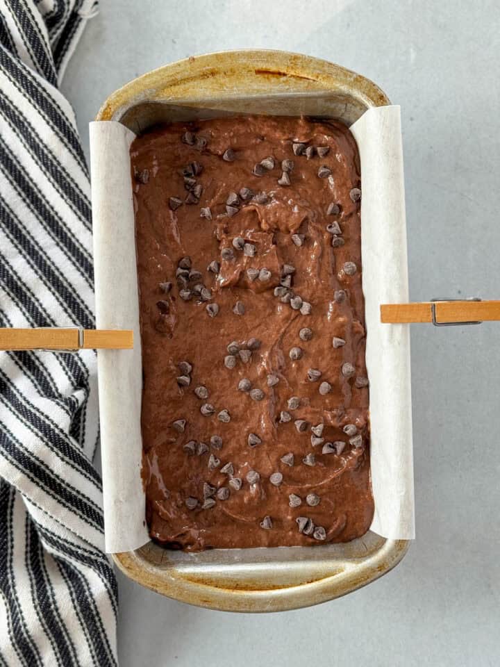 Bread batter spread evenly in parchment lined loaf pan with extra chocolate chips on top.