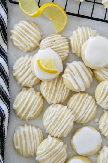 Lemon meltaway cookies in a staggered pile on parchment paper with lemon triangle garnishes.