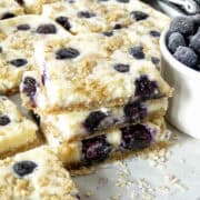 Blueberry cream cheese bars stacked next to bowl of blueberries.