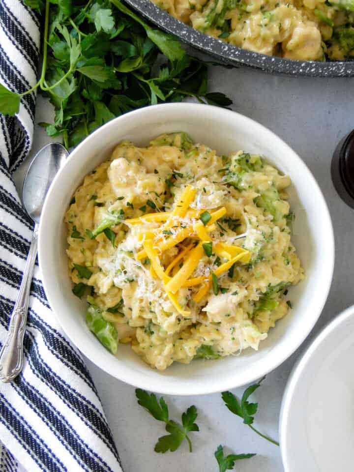Broccoli cheddar chicken orzo in white bowl with pork on side.