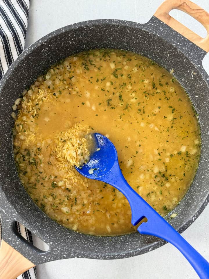 Orzo, spices and chicken broth added to cooked onions in skillet.