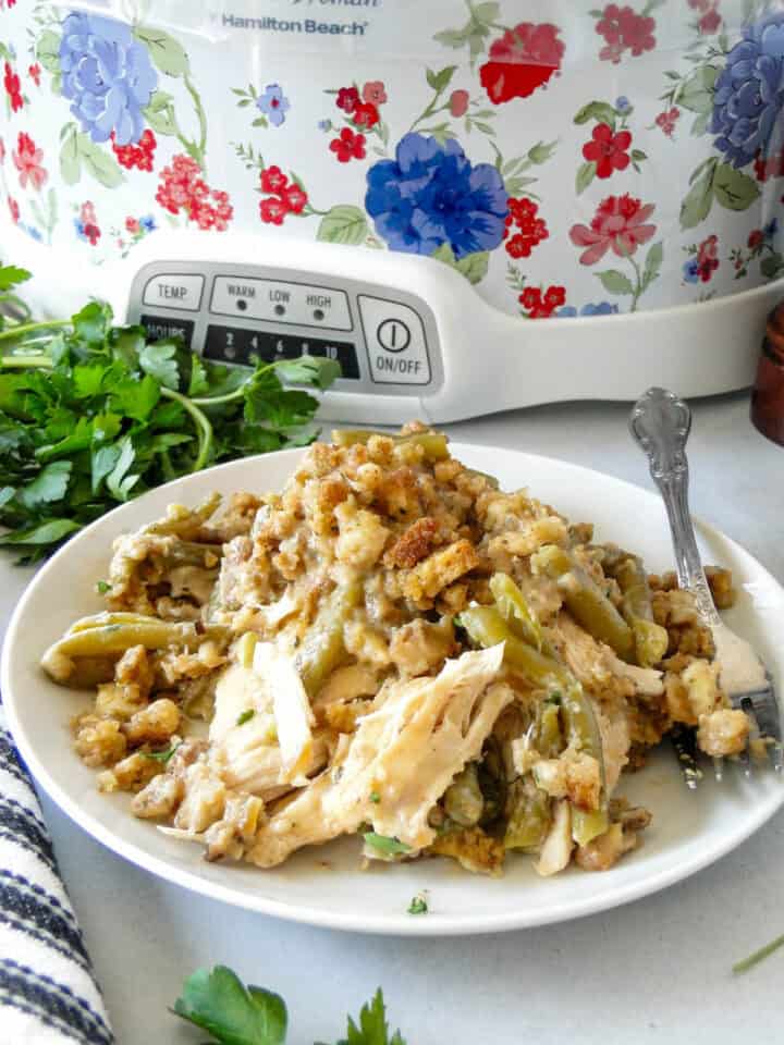 Side view of crock pot chicken and stuffing on plate with fork sitting in front of crock pot.