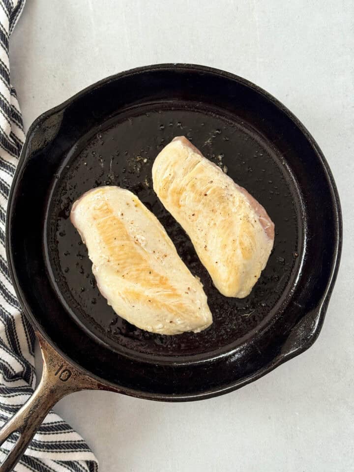 Chicken breasts in skillet seared on one side.