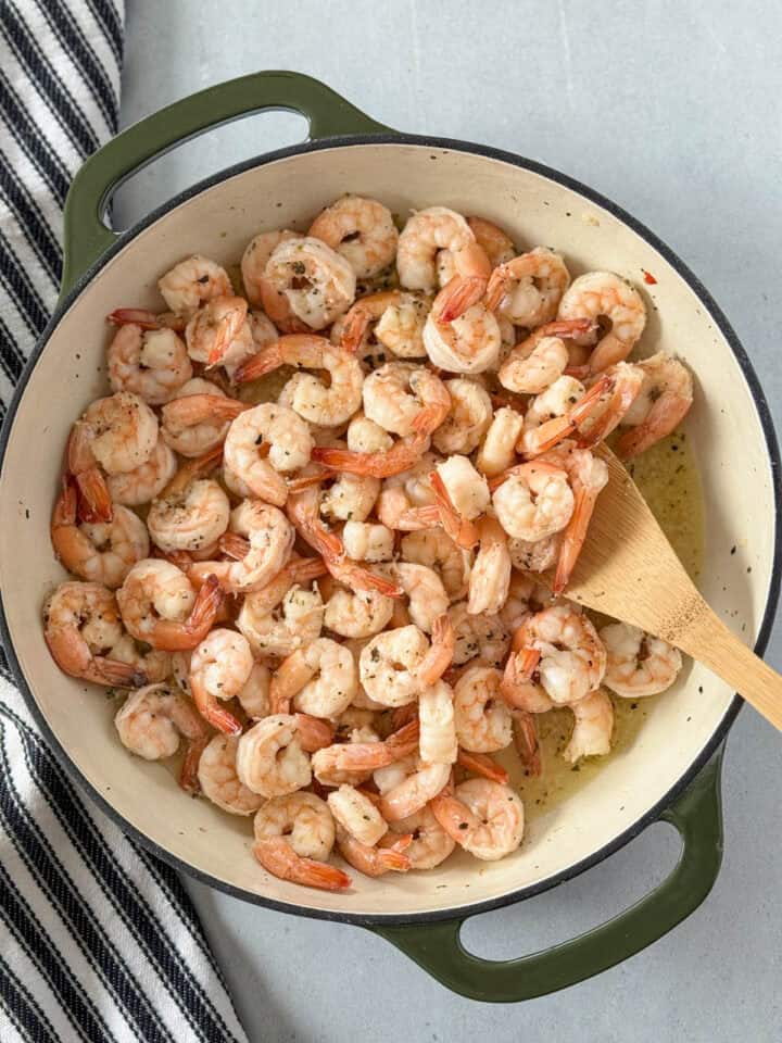 Sauteed shrimp with butter and garlic in skillet with wooden spoon.