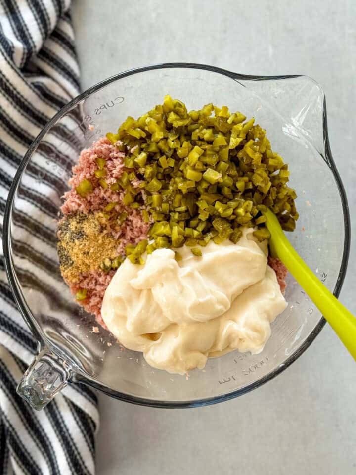 Ingredients added to minced ham in large glass mixing bowl with green spatula.
