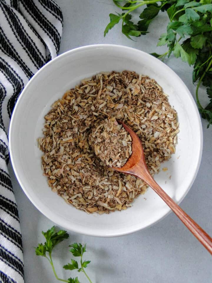 Homemade onion soup mix in white round bowl with mini wooden spoon.