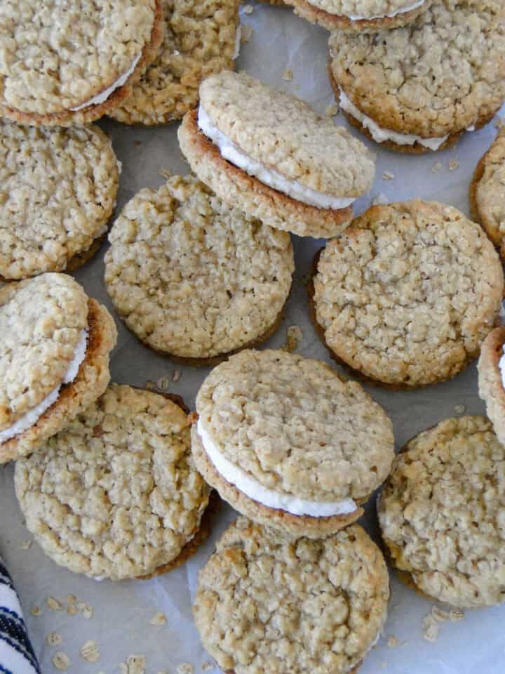 Homemade oatmeal crem pies scattered and layered on parchment paper.