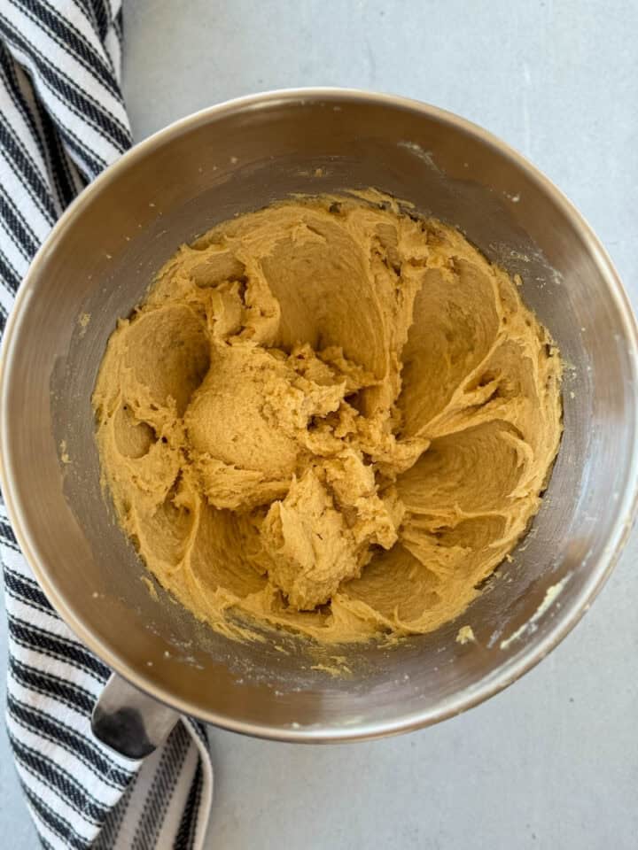 Eggs, honey and vanilla extract added to creamed butter and sugars in metal mixing bowl.