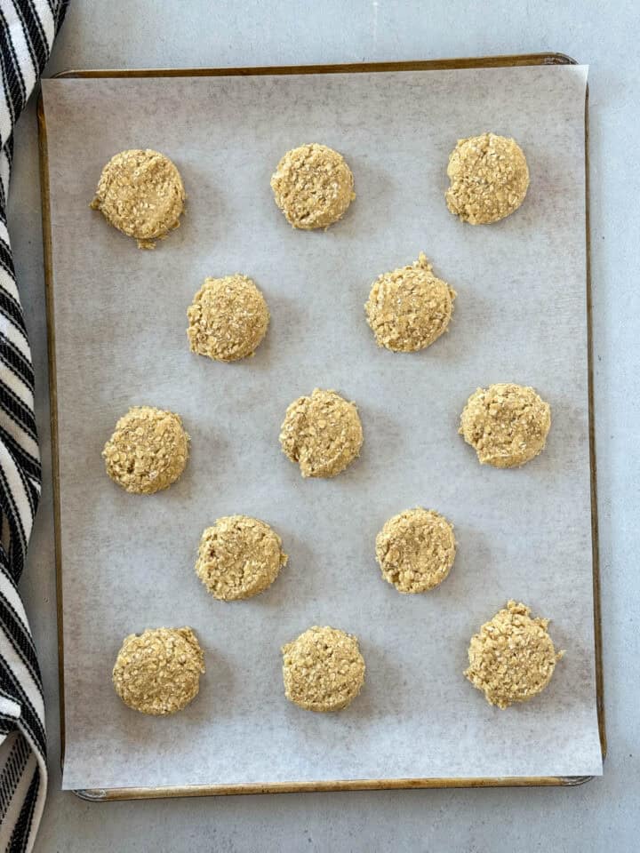 Cookie dough scoops slightly flattened on parchment lined cookie sheet.