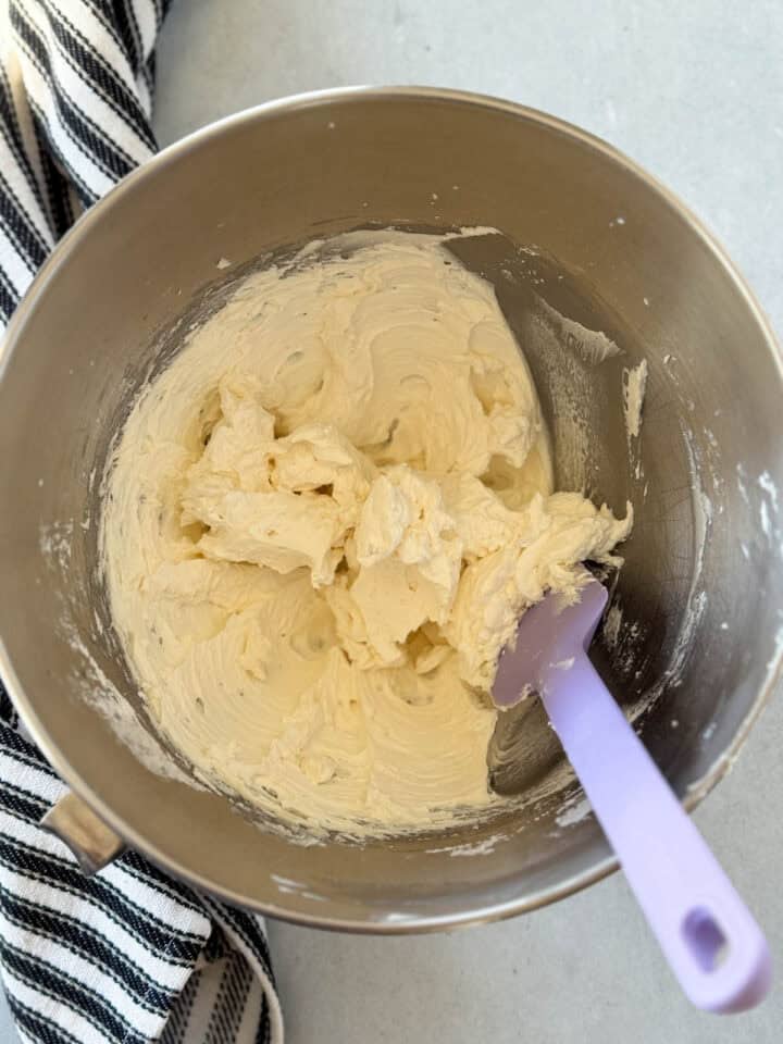 Creamy filling in metal mixing bowl with purple spatula.