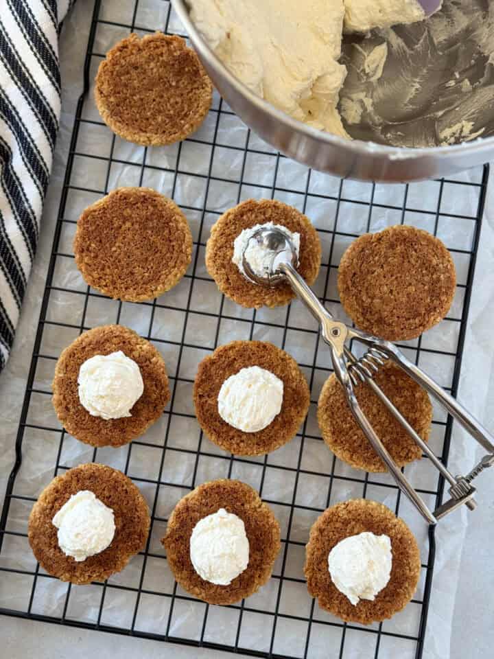 Buttercream filling scooped on bottoms of cookies on wire racks.