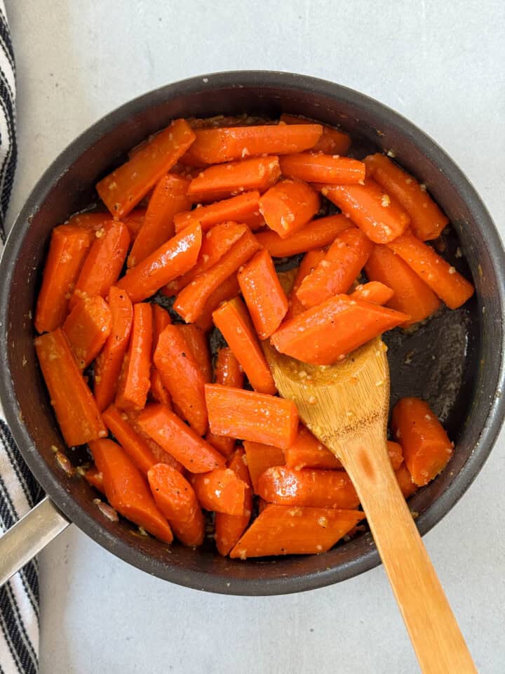 Honey added to cooked carrots in skillet with wooden spoon.