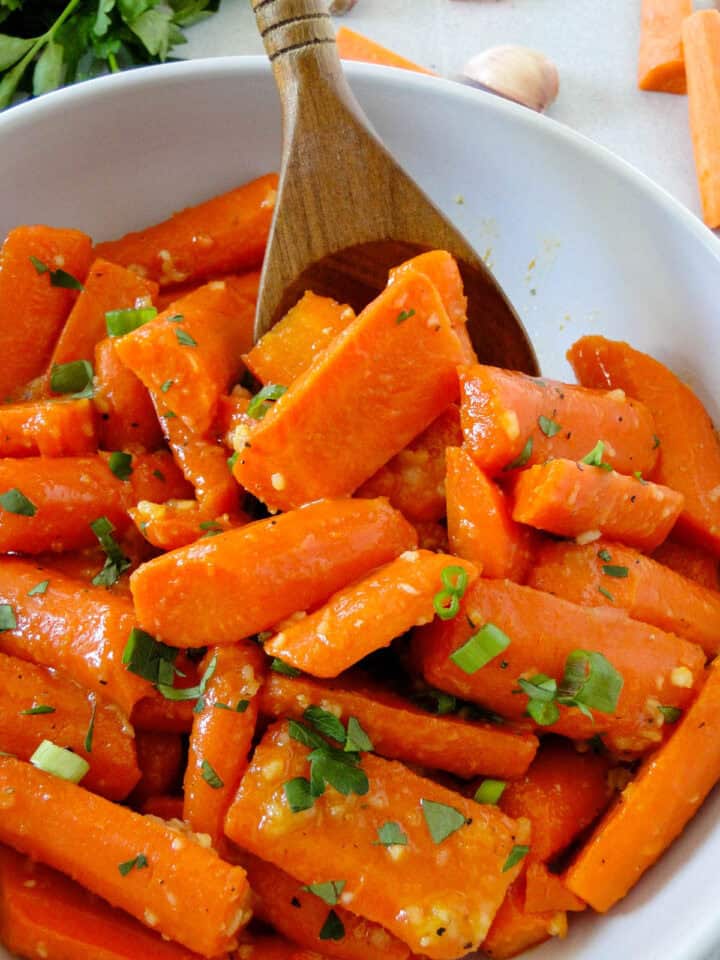 Close up side view of wooden serving spoon scooping honey garlic carrots from bowl.