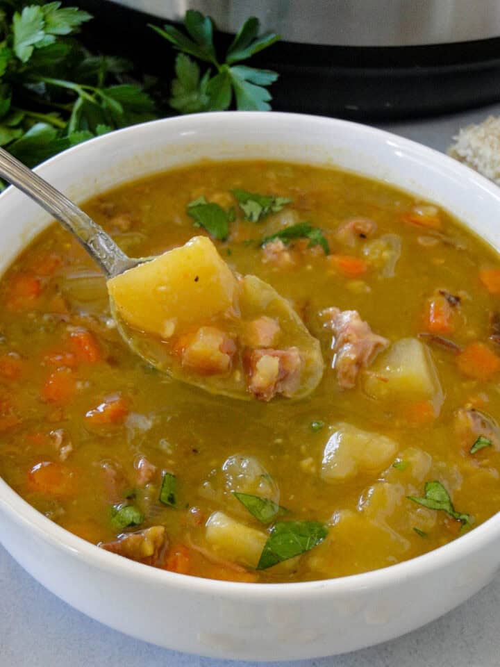 Close up side view of a spoonful of split pea soup with ham from bowl.