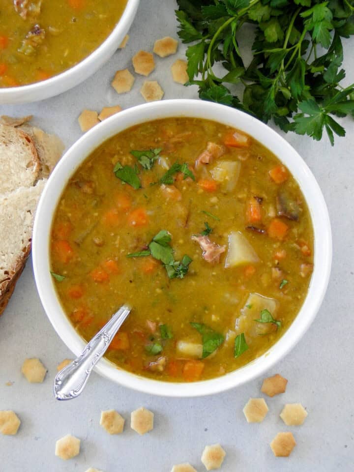 Top view of split pea soup with ham in white round bowl with spoon close by another filled bowl.