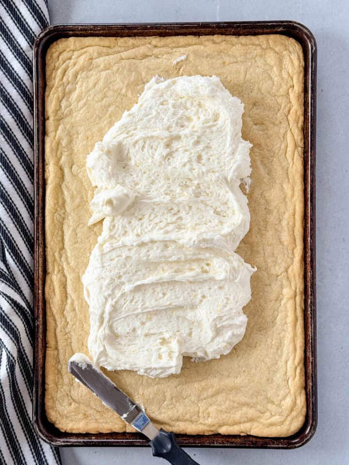 Frosting added on top of baked lemon cookie bars with offset spatula.