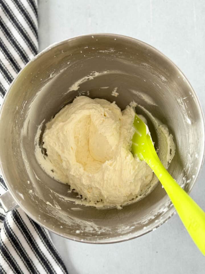 Lemon buttercream frosting whipped and in metal mixing bowl with green spatula.