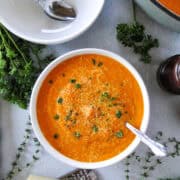 Creamy carrot soup in white round bowl with spoon and another bowl next to it.