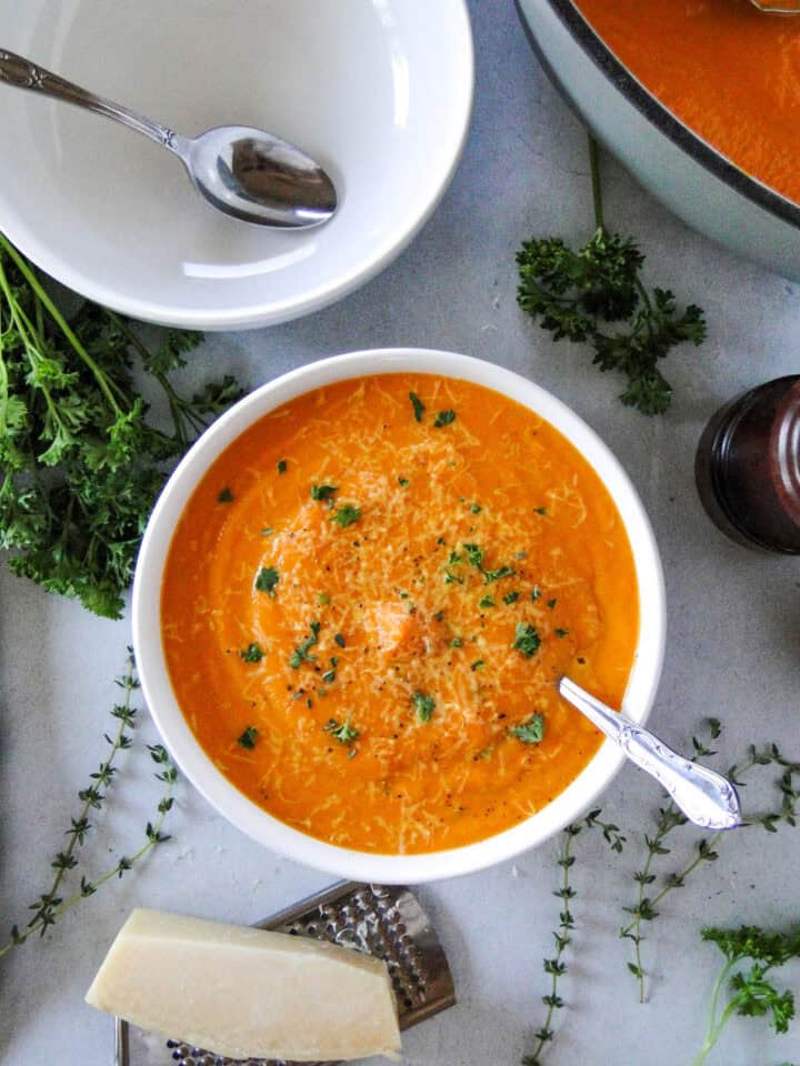 Creamy carrot soup in white round bowl with spoon and another bowl next to it.