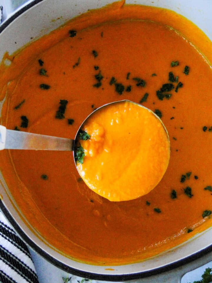Cream carrot soup in dutch with a ladleful being served.