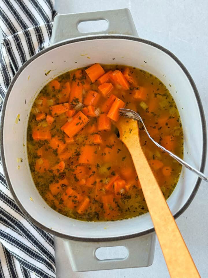 Cooked carrots in dutch oven with fork piercing one carrot to check for doneness.