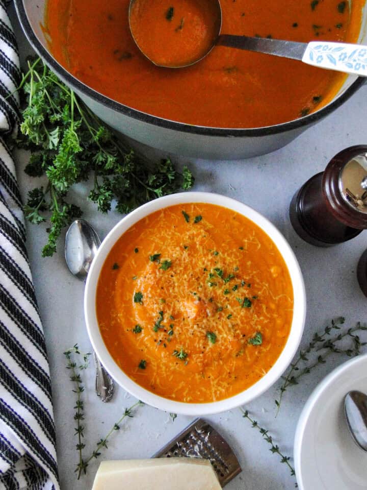 Bowl of creamy carrot soup sitting in front of dutch oven full of soup with ladle in it.