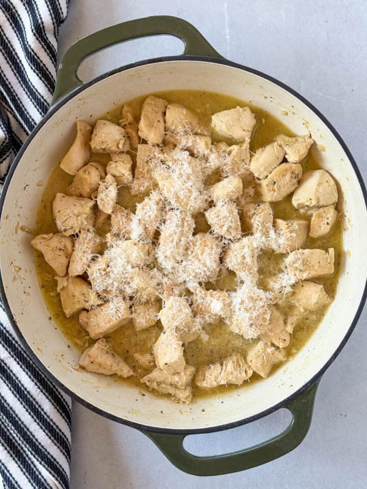 Parmesan cheese added to cooked chicken in skillet.