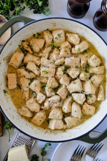 Top view of garlic butter chicken bites in skillet garnished with fresh parsley and serving spoon to the side.