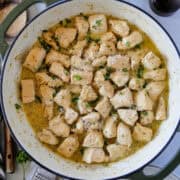 Top view of garlic butter chicken bites in skillet garnished with fresh parsley and serving spoon to the side.