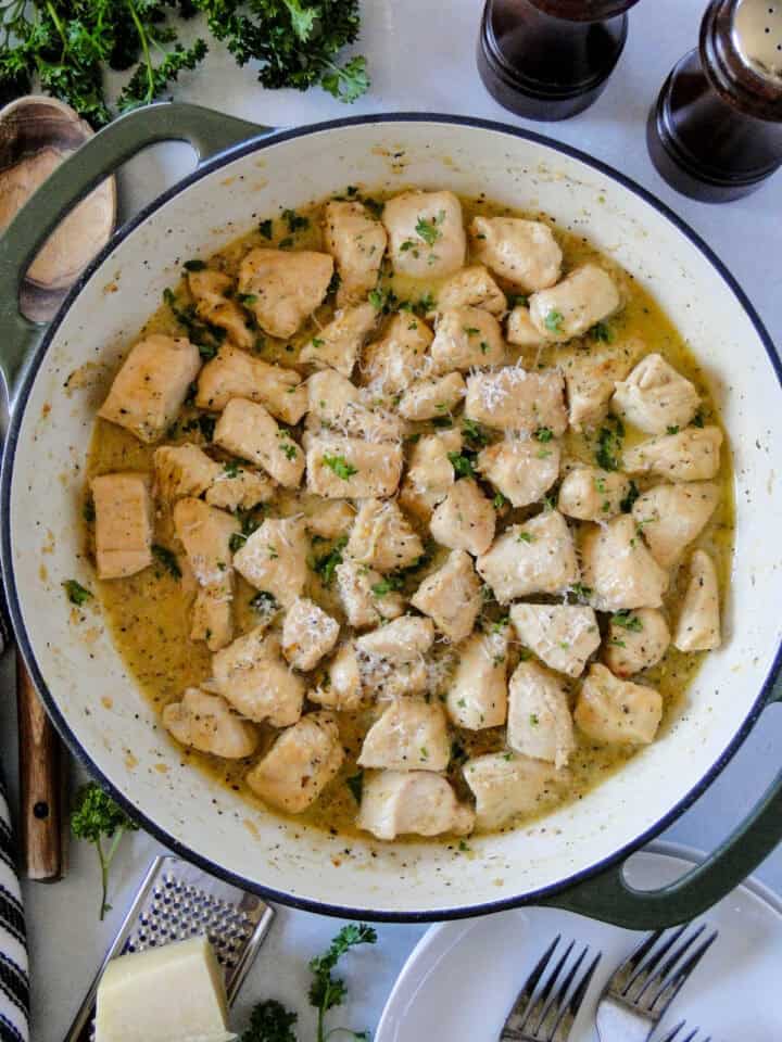 Top view of garlic butter chicken bites in skillet garnished with fresh parsley and serving spoon to the side. 