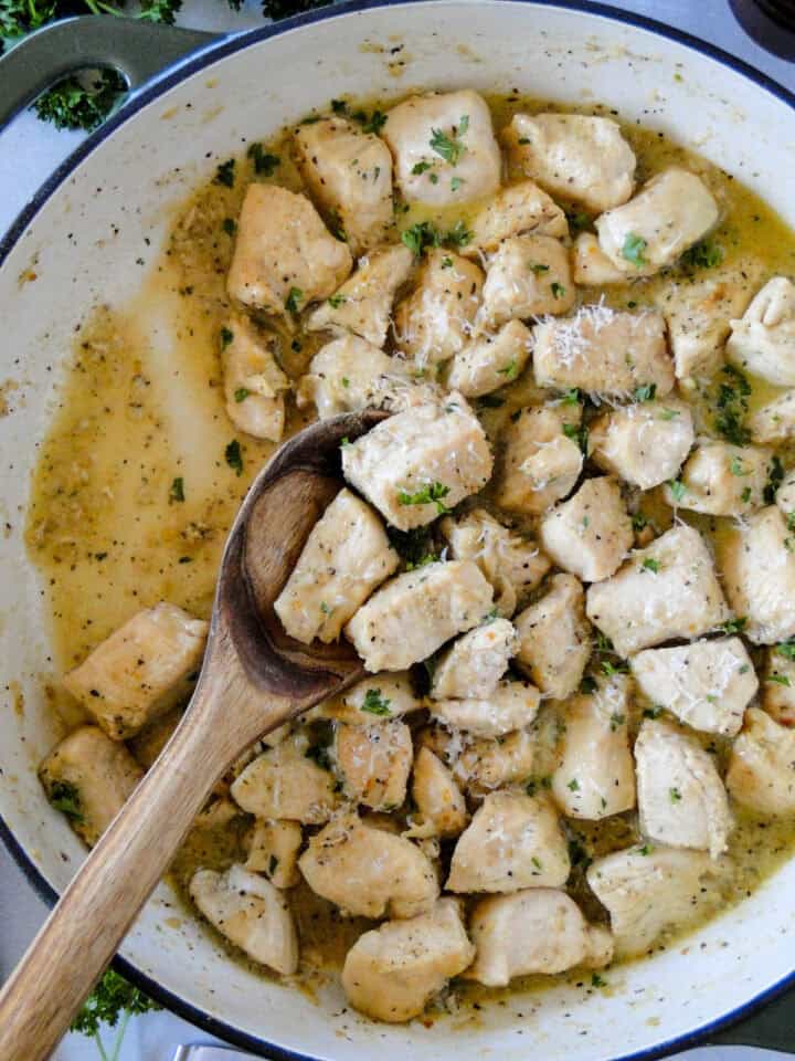 Top view of garlic butter chicken bites in skillet being served with wood serving spoon.
