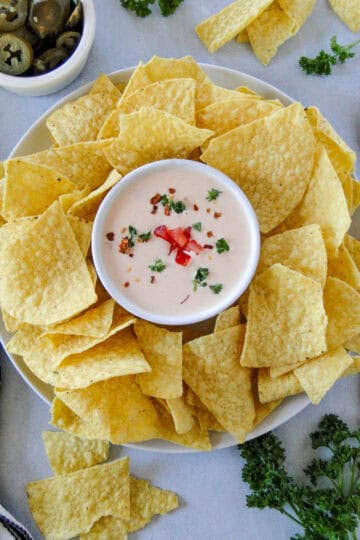 Top view of homemade queso dip in serving bowl surrounded by tortilla chips.