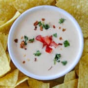 Close up top view of homemade queso dip in serving bowl garnished with extra tomatoes.
